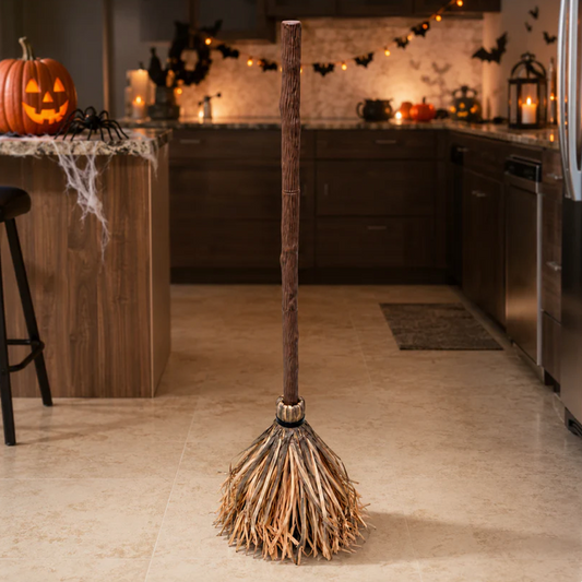 The Enchanted Flying Broom standing upright in a Halloween-decorated kitchen with a carved pumpkin, cobwebs, bats and candles